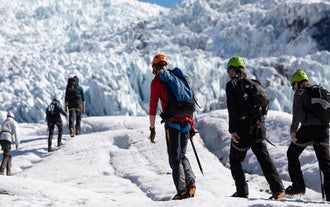 Three hikers hike on the massive icey field of Solheimajokull Glacier as part of a South Coast tour.