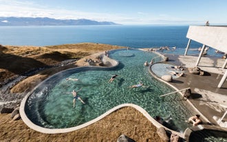 People relaxing in the warm infinity pools of GeoSea Geothermal Baths overlooking Skjalfandi Bay in North Iceland.