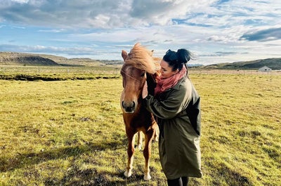 A woman strokes an Icelandic horse in a sunny field.