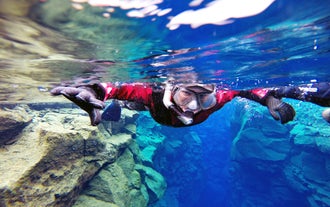 A person wearing a dry suit snorkels in the clear water of the Silfra fissure.