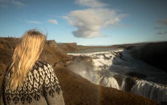 A woman wearing a traditional Icelandic sweater looks out over Gullfoss Waterfall in the Golden Circle.