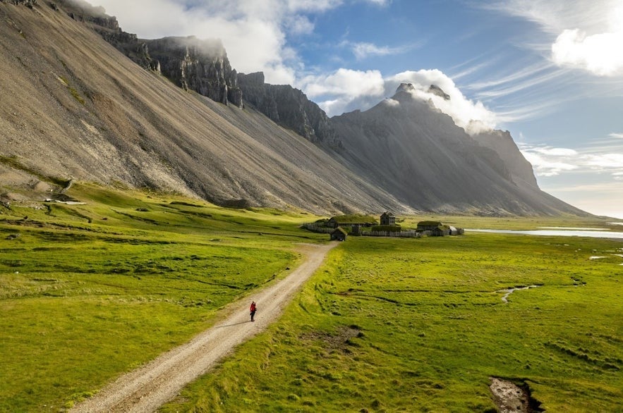 Person walking toward the Viking Village Film Set beneath Vestrahorn Mountain on Iceland’s scenic South Coast.