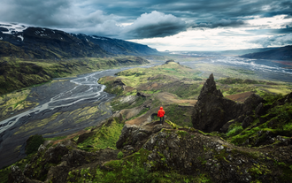 Hiker in red jacket admiring the dramatic, glacial river-filled landscape of the Icelandic Highlands.