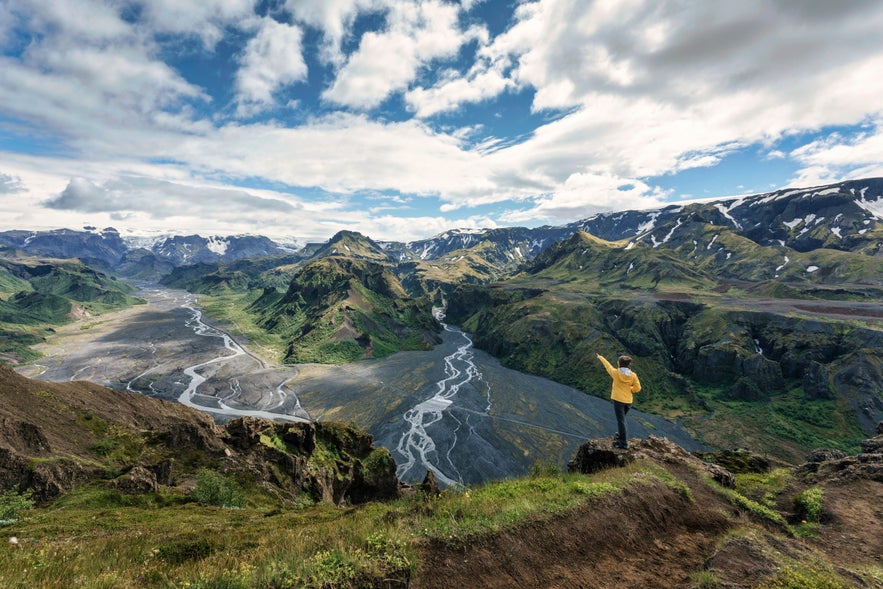 A woman hiker wearing a yellow jacket standing on a viewpoint at Thorsmork in Iceland’s Highlands.