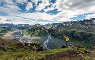 A hiker standing on a cliff, admiring the expansive glacial valleys and mountains from the Fimmvorduhals Trail.