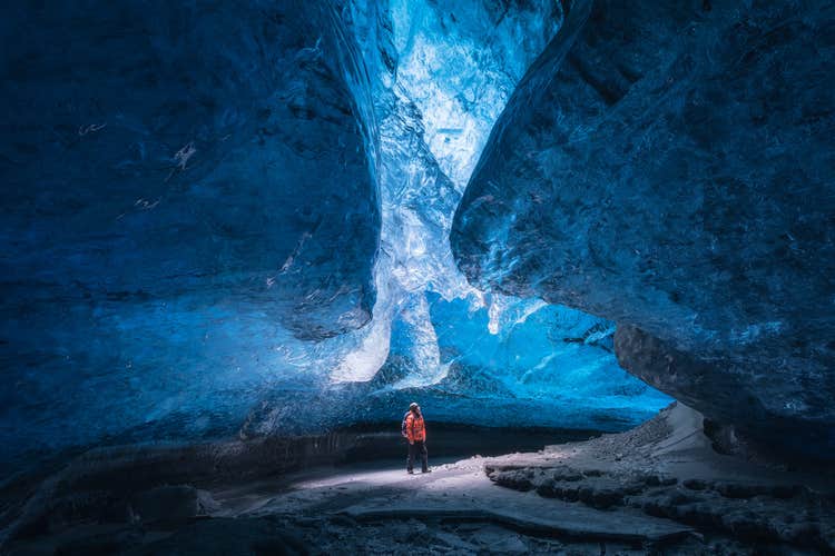 A traveler looks up to see the beautiful ceiling of a blue ice cave in Iceland.