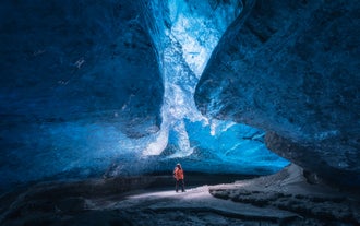 A traveler looks up to see the beautiful ceiling of a blue ice cave in Iceland.