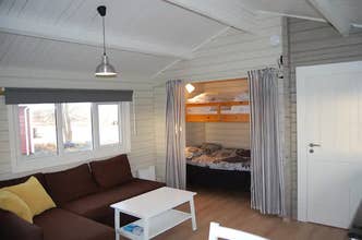 Main room at Moar Cottage with sleeper sofa, coffee table, and a double bed with single bunk behind privacy curtains.
