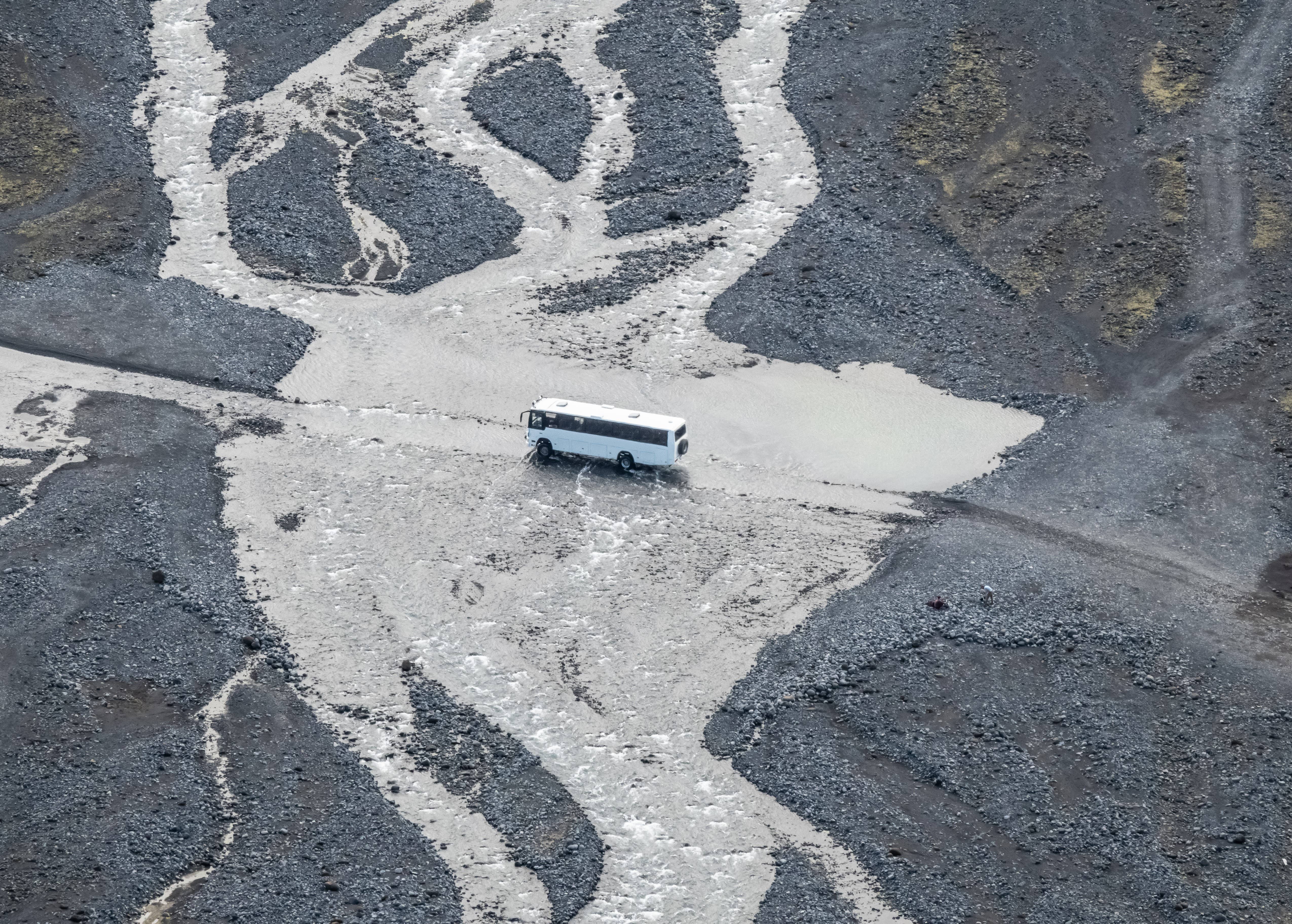 A bird's-eye view of a highland bus crossing a shallow river in South Iceland.