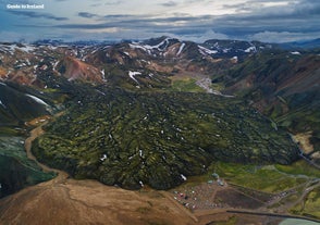 A top view of Landmannalaugar in the Icelandic Highlands, featuring a vast lava filed, mountains, and the basecamp.