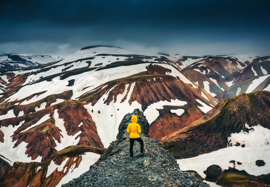 Vaeltaja ihailee Landmannalaugarin lumilaikkuisia vuoria Islannissa.
