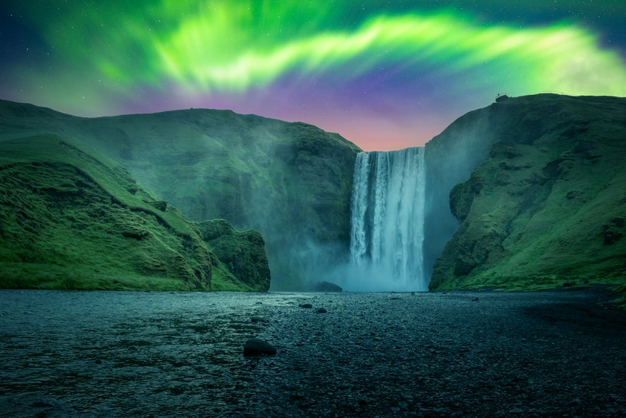Green aurora light behind famous Skogafoss waterfall on Skoga river.
