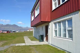 Side exterior view of Framtid Apartments and Holiday Homes with a red upper level and white lower level with grass out the front