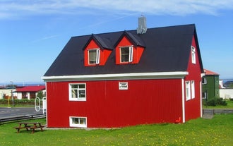 An exterior view of the red house at Grundarfjordur HI Hostel with a picnic table on the grassy surrounding area on a bright, bl