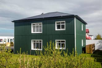 An exterior view of the green house at Grundarfjordur HI Hostel with grass and plants in front.