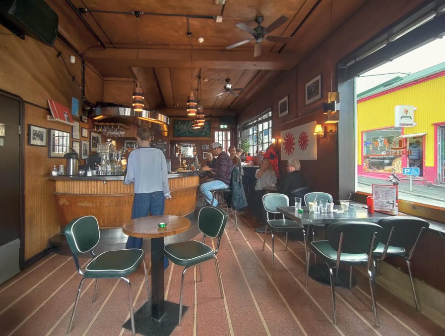 Cozy interior of Prikið café in Reykjavik with wood-paneled walls, framed photos, and customers enjoying a relaxed afternoon