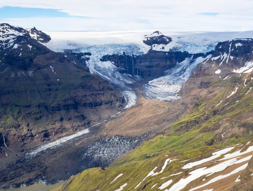 Aerial view of a glacier tongue descending between green and snow-streaked mountains in Skaftafell