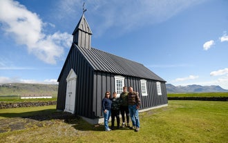 A family of four people standing outside Budakirkja, the black colored church.