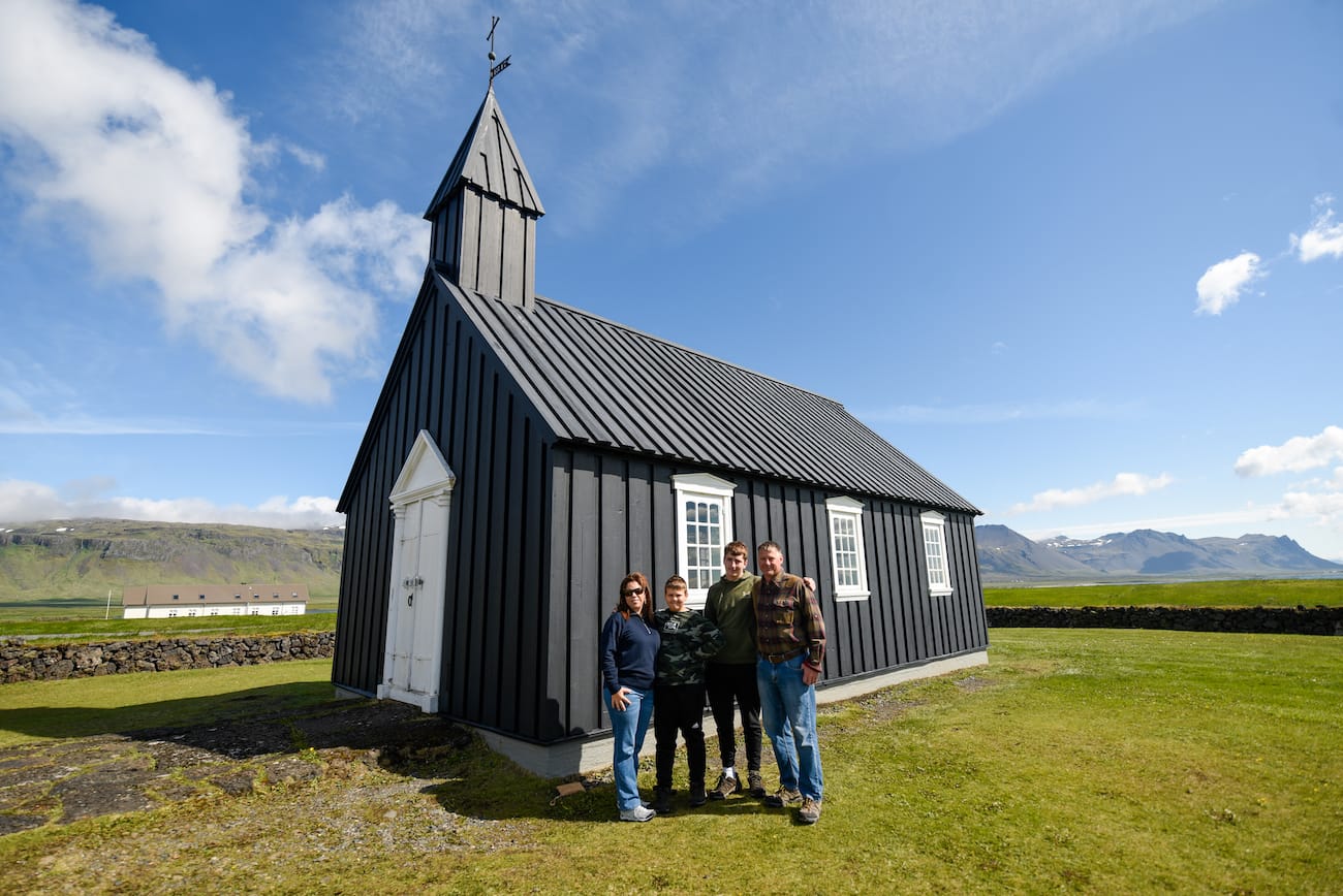 Una familia de cuatro personas posa junto a la iglesia negra de Budakirkja.