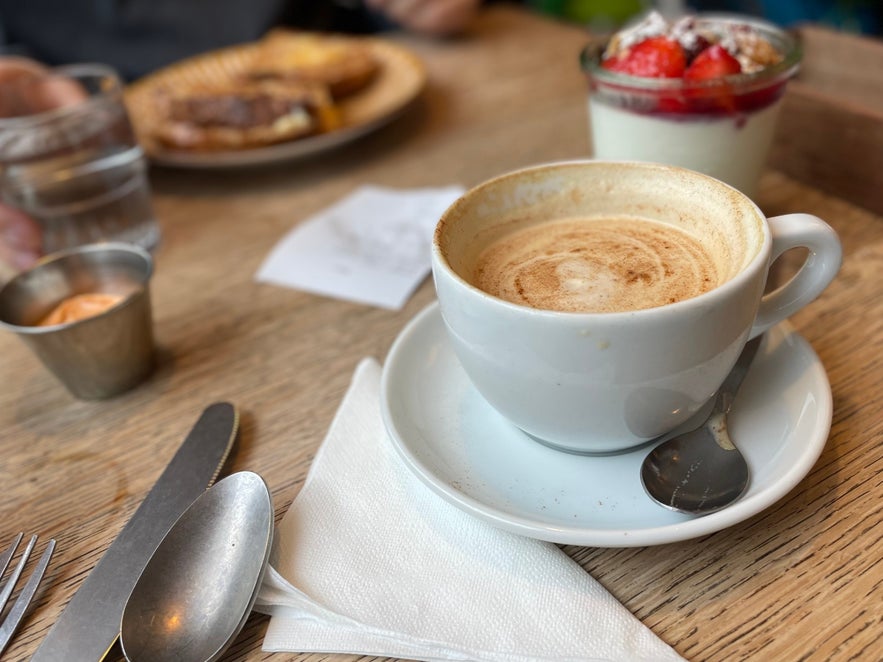 A warm cup of coffee and deserts on a wooden table in a cafe in Vik, Iceland.