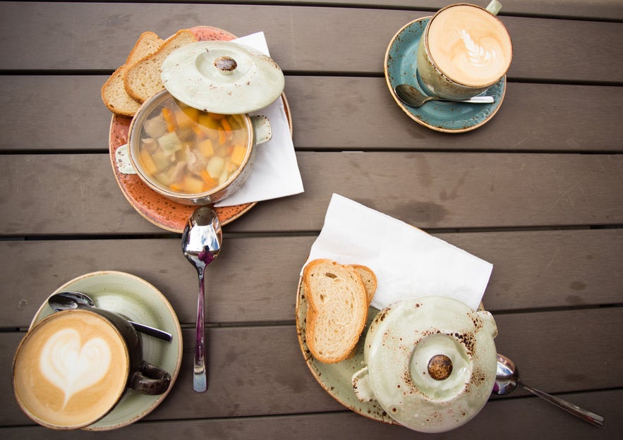 Cups of warm coffee, pastries, and an Icelandic dish on a wooden table in a cafe in Vik.