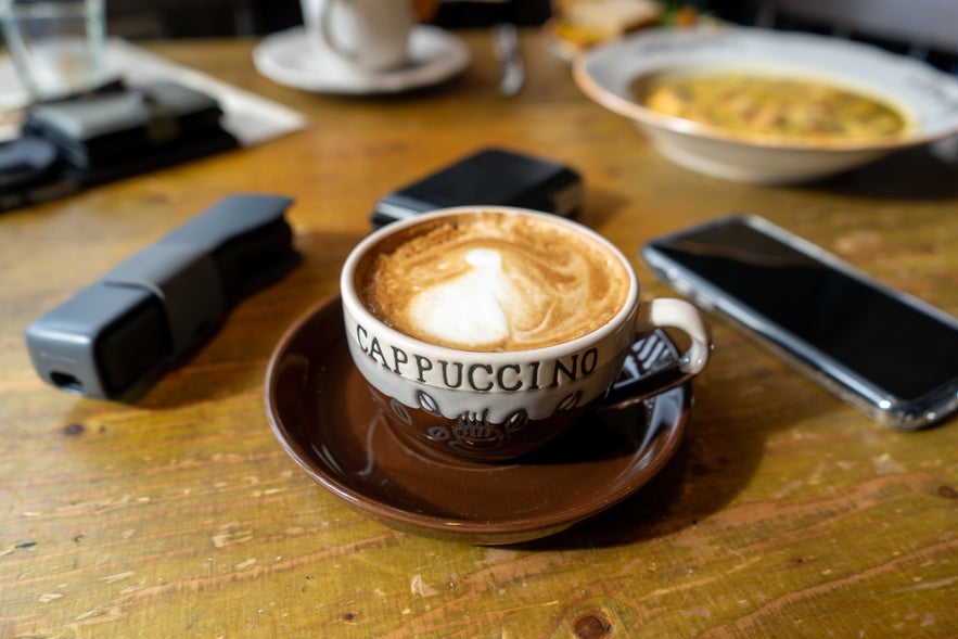 A warm cup of cappuccino on a wooden table in a cafe in Vik, Iceland.
