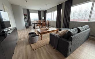 Salon spacieux de l’appartement Heima at Selfoss avec canapé gris, table basse en bois et coin repas.