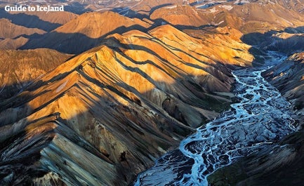 A bird's eye view of Landmannalaugar shows the picture-perfect contrasts of the sun shining over caramel-colored mountain peaks and glacial rivers weaving through the valley below.