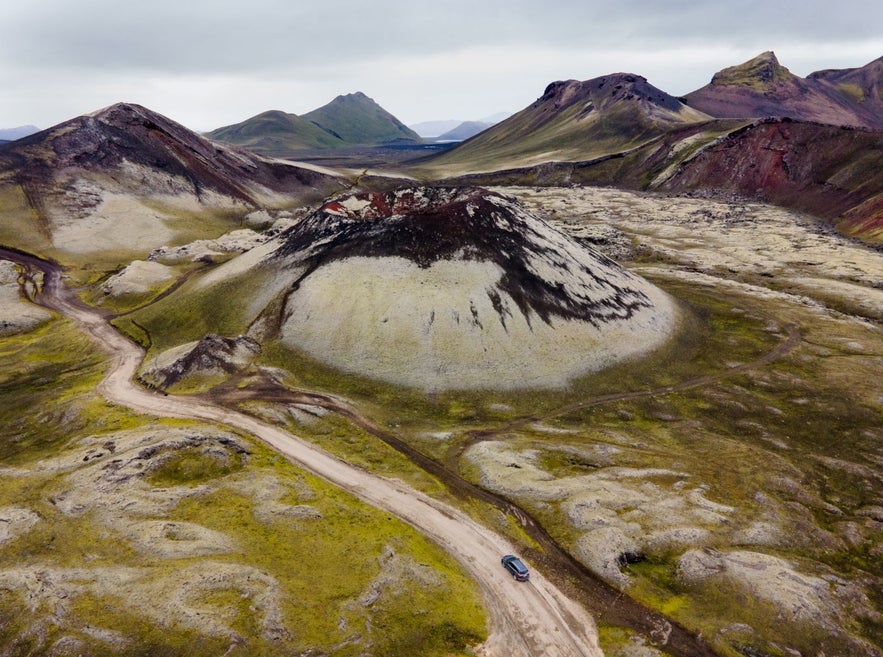 A 4x4 vehicle driving in Iceland's Highlands next to a moss covered volcanic crater