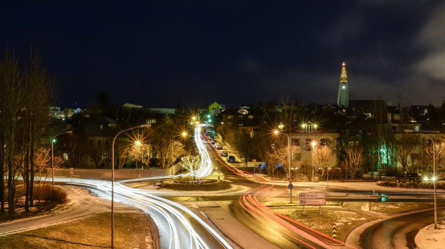Driving in Iceland through a Reykjavik roundabout at night with light trails and Hallgrimskirkja in the distance.