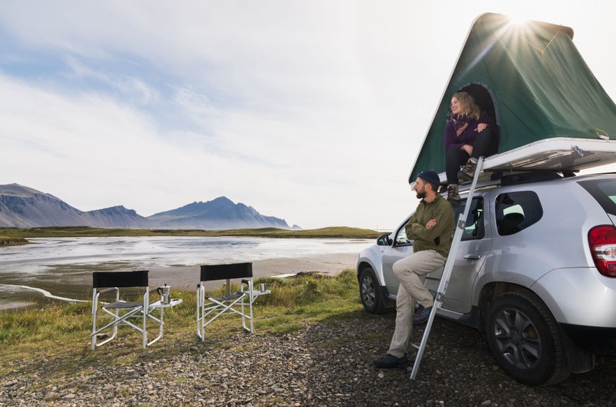 A couple traveling in Iceland with a roof tent and a jeep, admiring the view of Mount Vestrahorn