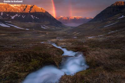 Une petite mais magnifique rivière dans les Fjords de l'Ouest, avec de la neige sur les montagnes environnantes en été et un superbe arc-en-ciel au loin sous le soleil.
