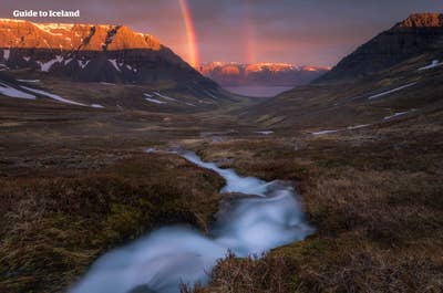 Une petite mais magnifique rivière dans les Fjords de l'Ouest, avec de la neige sur les montagnes environnantes en été et un superbe arc-en-ciel au loin sous le soleil.