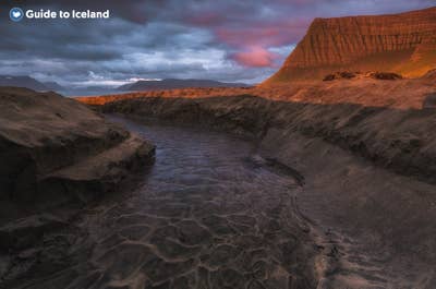 Une rivière des Fjords de l'Ouest serpente dans un paysage sauvage, sous un ciel nuageux teinté de rose.