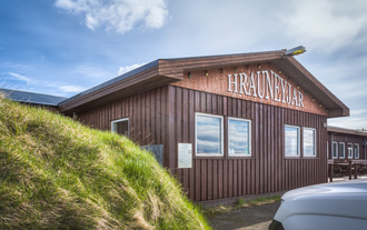 Highland Center Hrauneyjar lodge with wooden facade beside a grassy mound under clear skies.