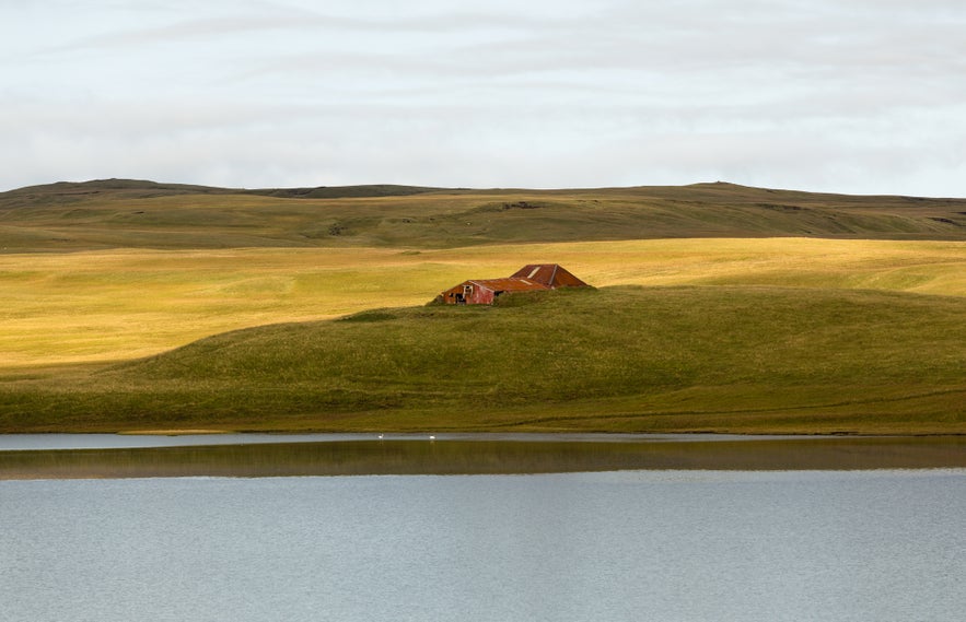 A scenic view of a barn across a lake in Kirkjubaejarklaustur.