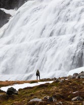 A person stands near the bottom of Dynjandi Waterfall in Iceland.