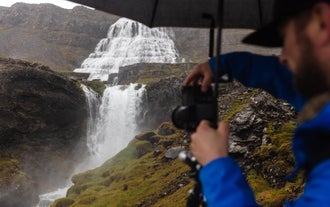 A person holds an umbrella and takes a photo of the Westfjords' Dynjandi Waterfall.