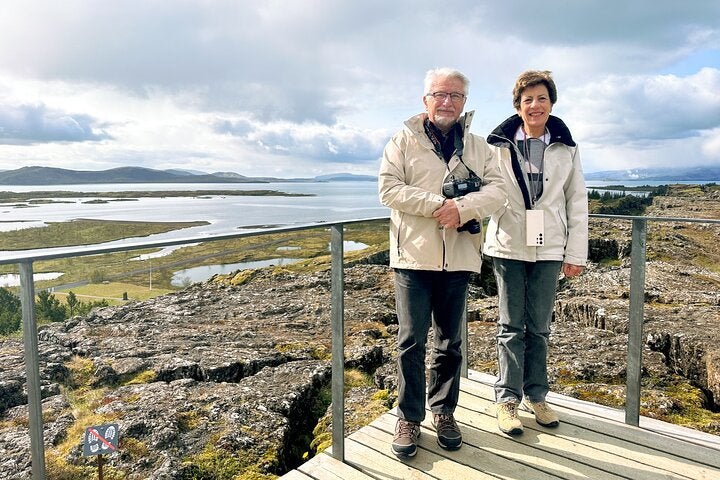 A couple poses for a photo on a viewing platform overlooknig the unique geography of Thingvellir National Park on a Golden Circle tour.