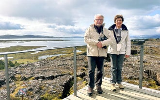 A couple poses for a photo on a viewing platform overlooknig the unique geography of Thingvellir National Park on a Golden Circle tour.