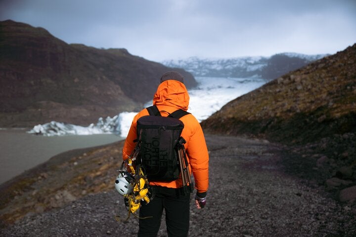 A hiker with a backpack and hiking essentials such as a rope and helmet walk toards the edge of Solheimajokull Glacier.