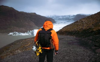 A hiker with a backpack and hiking essentials such as a rope and helmet walk toards the edge of Solheimajokull Glacier.