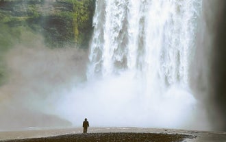 A man looks extremely tiny at the base of the mighty Skogafoss Waterfall, a famous stop on many South Coast tours.