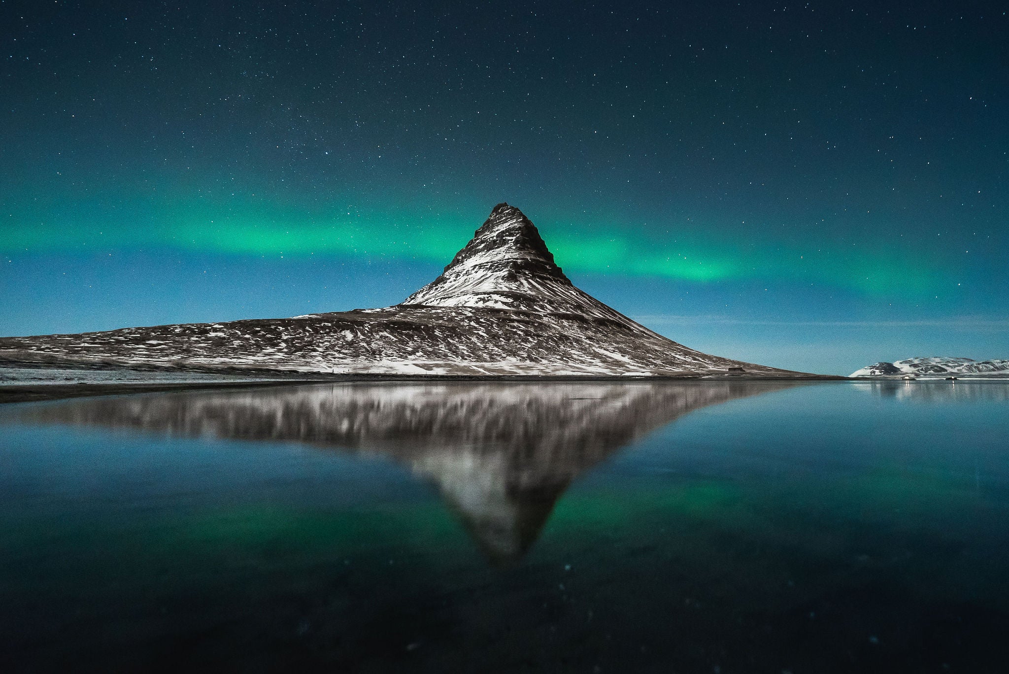Aurora borealis above Kirkjufell Mountain in Iceland with reflections on the still water.