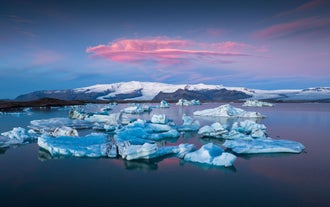 Icebergs drift across Jokulsarlon Glacier Lagoon with Vatnajokull Glacier glowing under a pink sunset sky.
