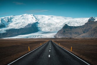 Road leading toward Vatnajokull Glacier with rugged mountains and snowy peaks along Iceland’s South Coast.