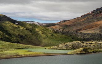 Green moss slopes and a turquoise lake in Landmannalaugar’s volcanic landscape.