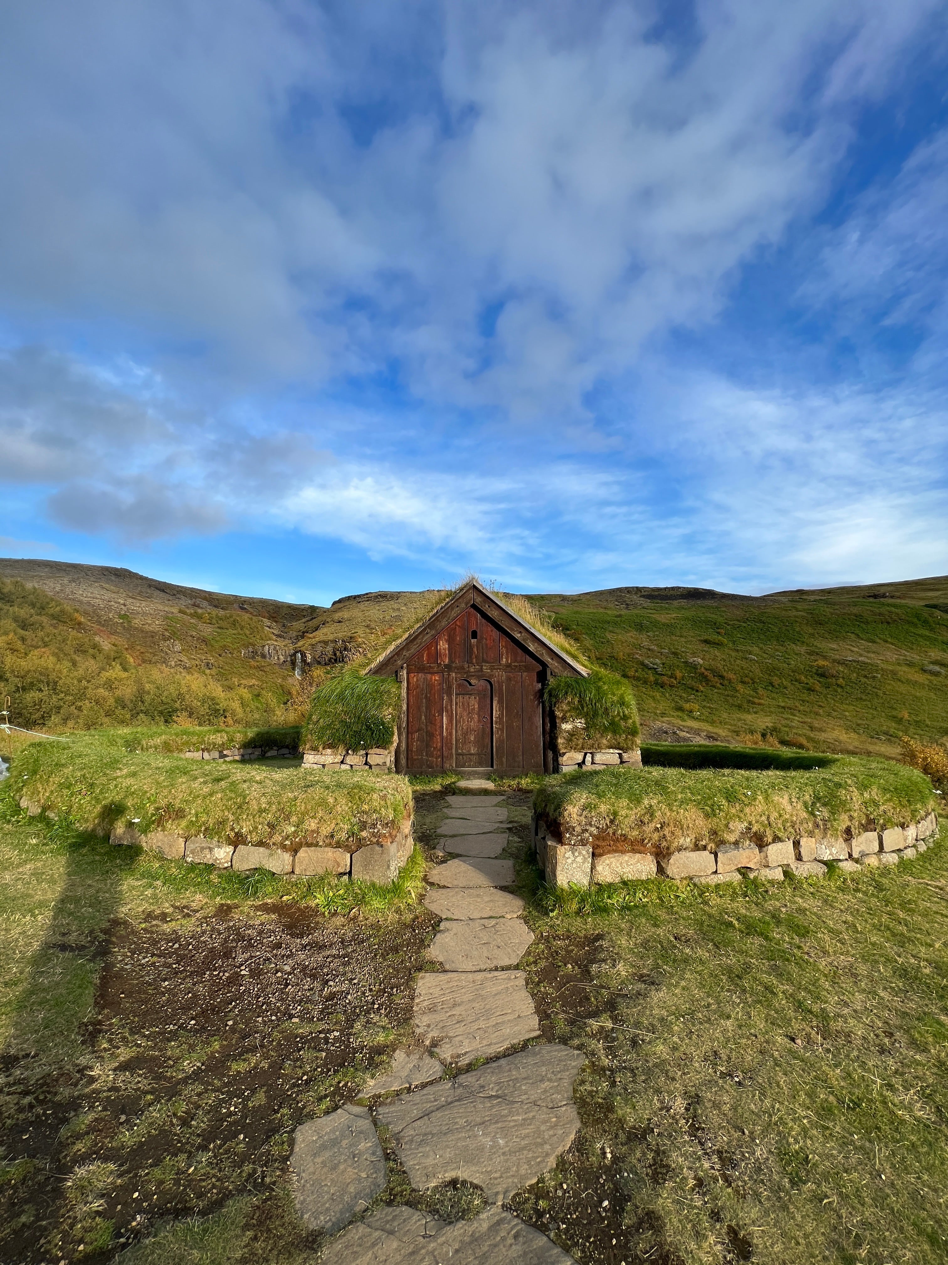 Reconstructed turf house at Stöng farm in the Highlands, surrounded by green hills and stone walls.
