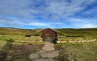 Reconstructed turf house at Stöng farm in the Highlands, surrounded by green hills and stone walls.