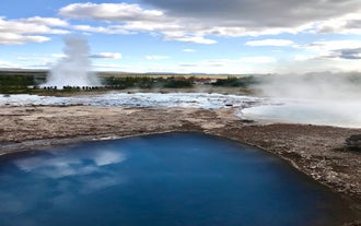 Strokkur geyser erupting beside steaming hot springs in the geothermal valley.